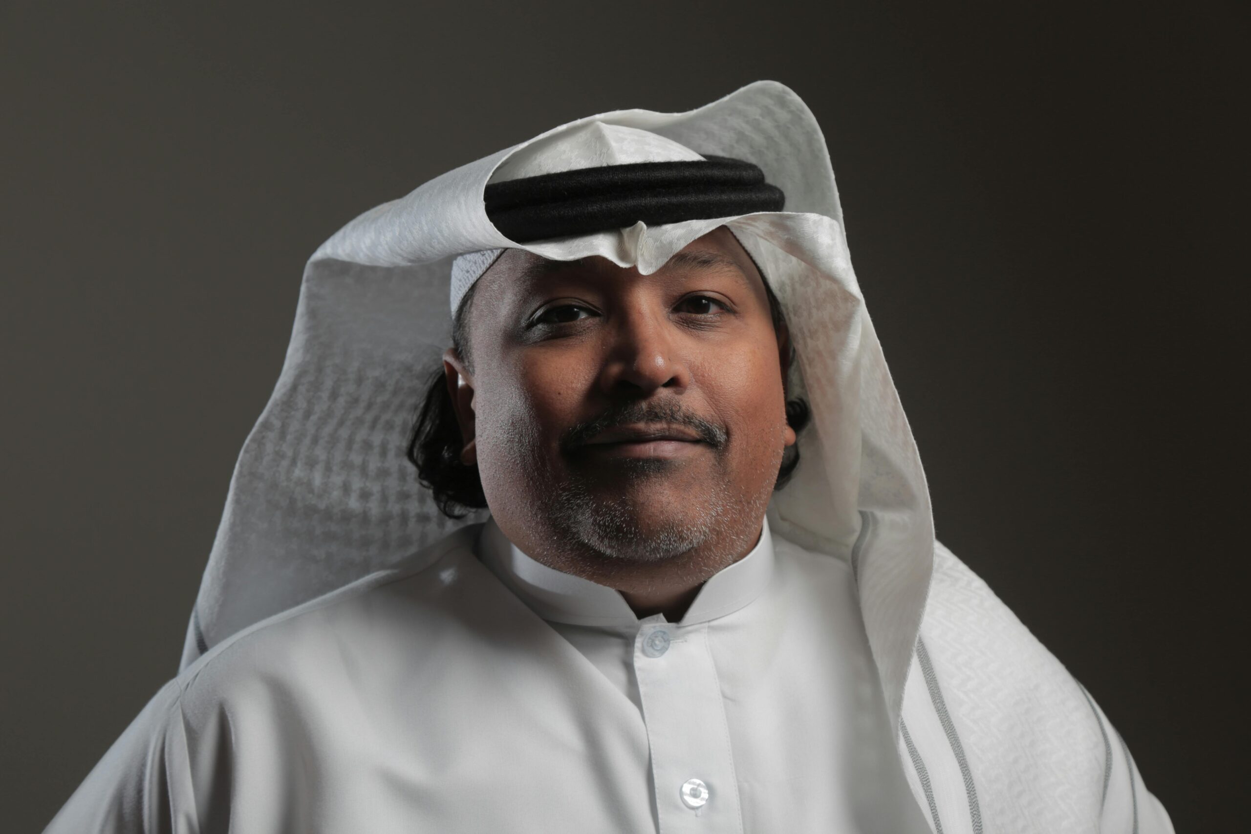 Home Portrait of a middle-aged Arabic man in traditional attire with a neutral background.